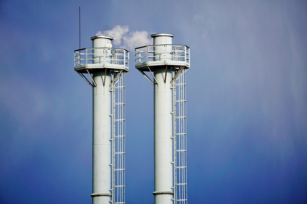 Dos chimeneas metálicas con plataformas y escaleras de servicio sobre cielo azul.